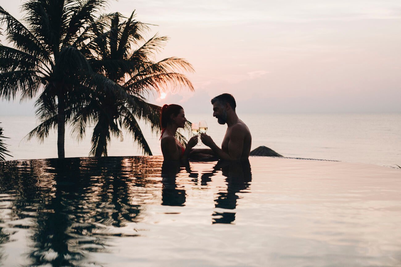 couple in pool holding drinks with sunset in the back